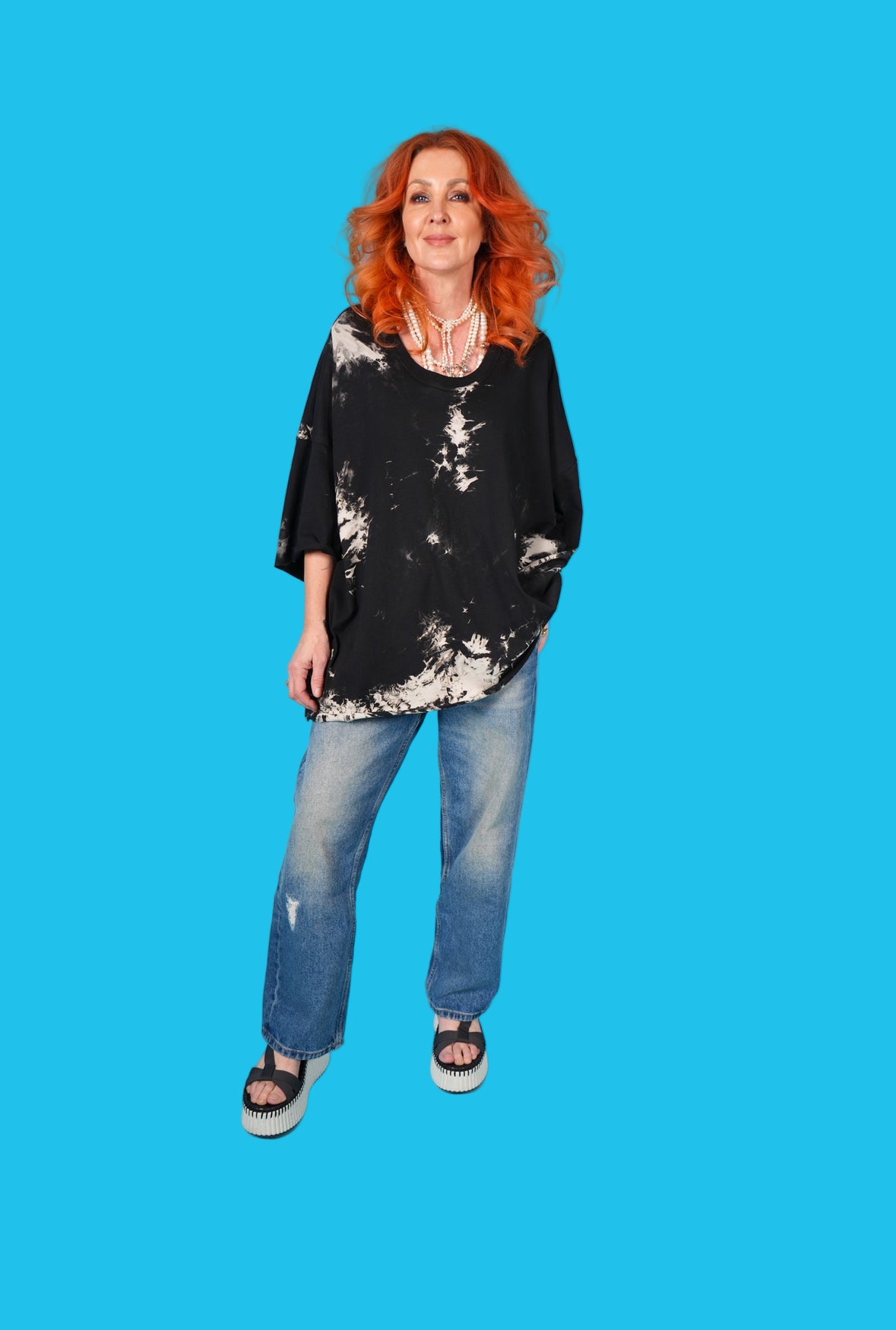 Woman with red hair wearing a black and white top and blue jeans on a blue background