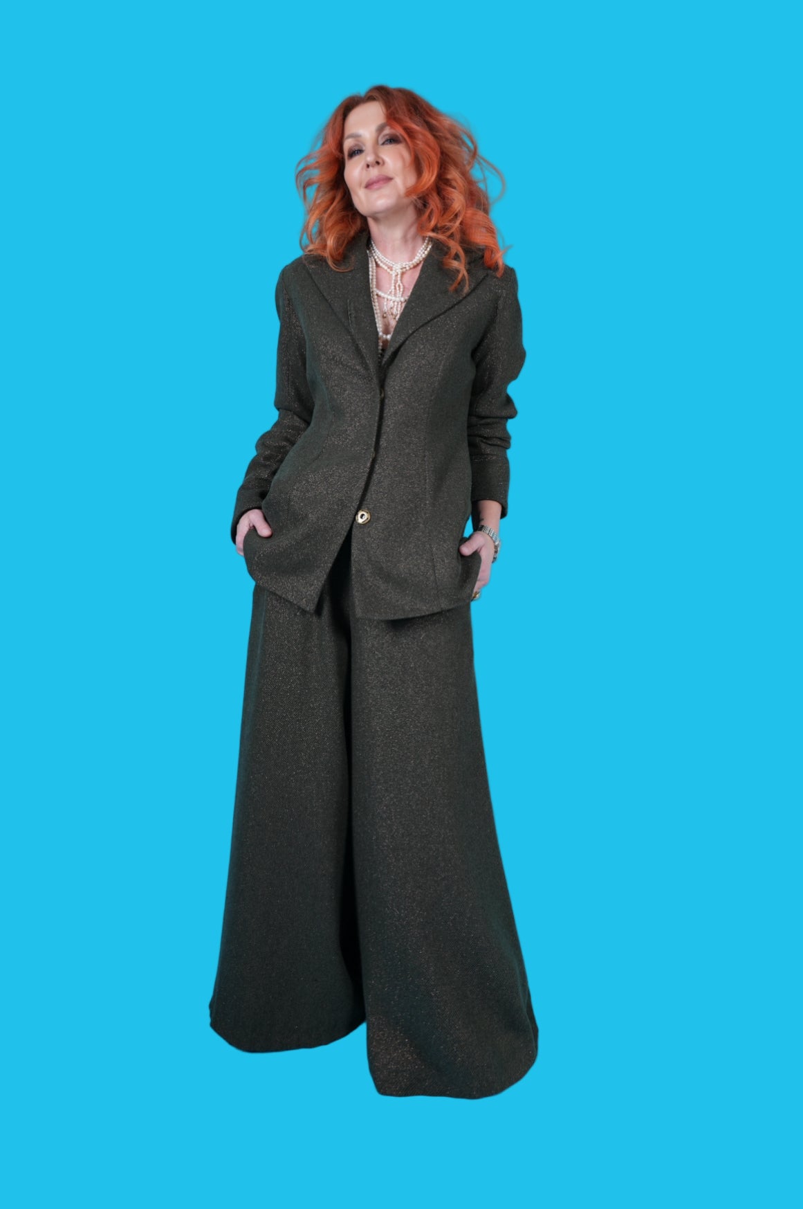 Person wearing a long dark coat and wide-leg pants against a blue background