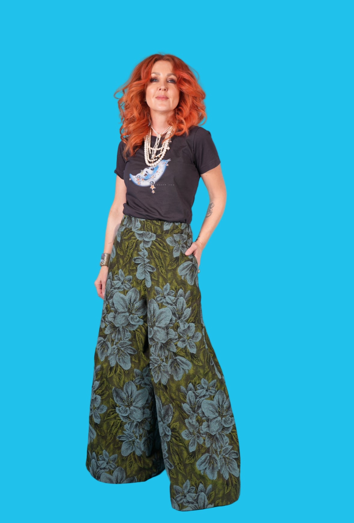 Woman wearing a black t-shirt with a graphic design and green floral pants against a blue background